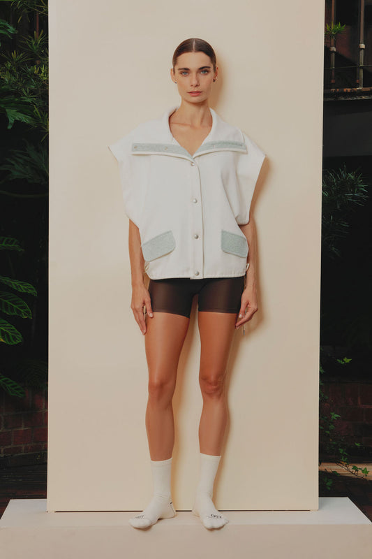 Chaleco deportivo semi oversized en algodón crudo, con cuello y solapas en tela ovejera baby blue y cordones ajustables del mismo tono.