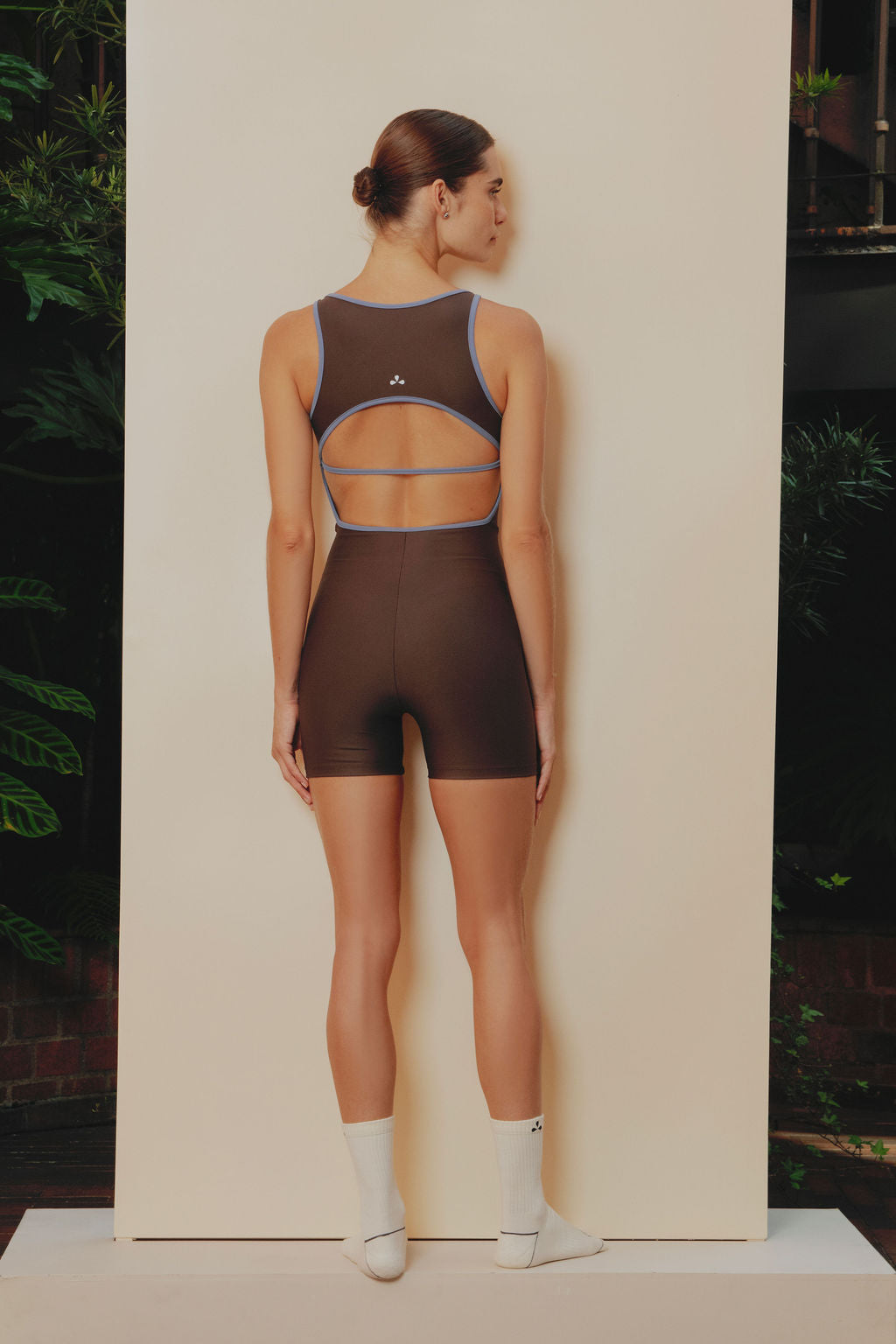 Gasset- Enterizo deportivo corto en color café con abertura en la espalda, tira y sesgos azul claro que recorren y perfilan la silueta.